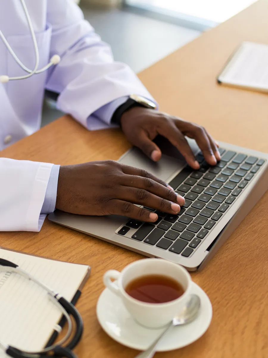 A dermatologist's hands at a laptop with a stethoscope on the desk